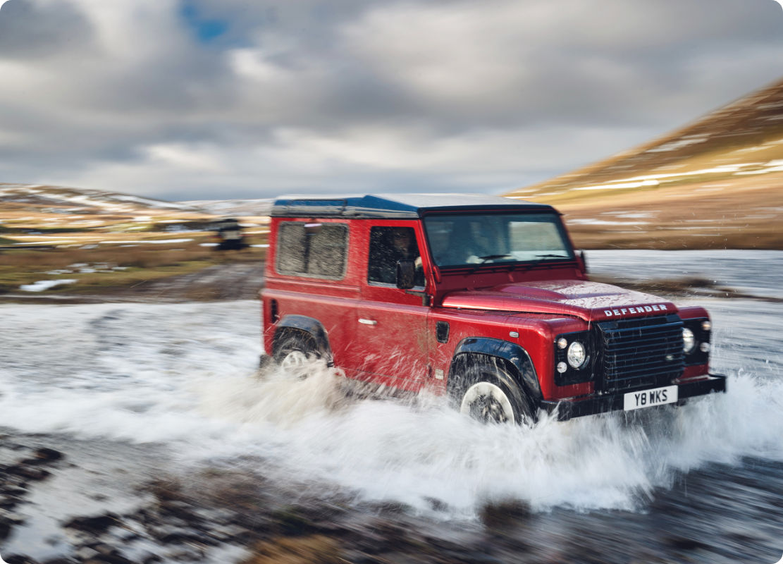Red Defender driving through water.
